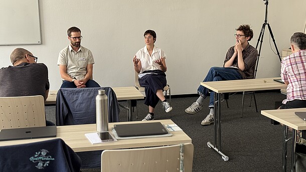 View of panelists during workshop, with chairs and tables and some audience members in the foreground.